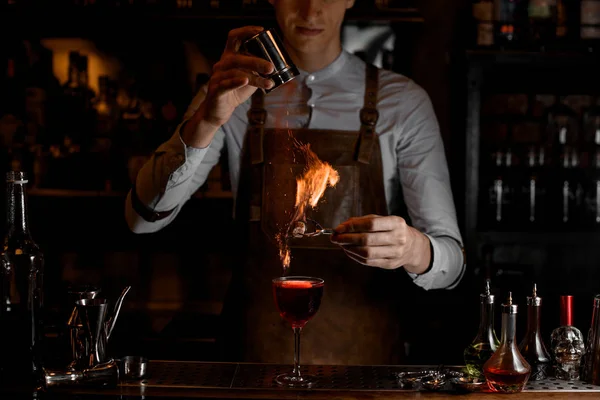 Cantinero añadir especias para una decoración en el fuego por encima de un delicioso cóctel rojo en el vaso — Foto de Stock