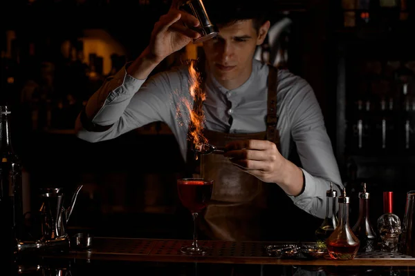 Varón camarero añadir especias para una decoración en el fuego por encima de un delicioso cóctel rojo en el vaso — Foto de Stock