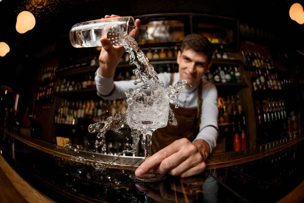 Fischaugenschuss lächelnder männlicher Barkeeper, der einen Cocktail aus dem Messbecher ins Glas gießt — Stockfoto