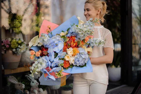 Жінка тримає величезний букет ніжно-блакитних і помаранчевих квітів — стокове фото