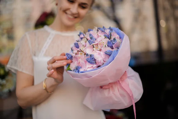Menina sorridente segurando um buquê de luz suave rosa e pequenas flores azuis — Fotografia de Stock