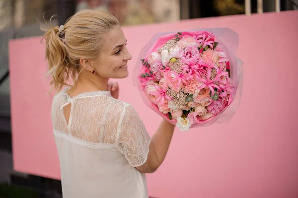 ผู้หญิงที่ยิ้มถือช่อดอกไม้ฤดูใบไม้ผลิของดอกไม้สีชมพูอ่อนและสีขาว — ภาพถ่ายสต็อก