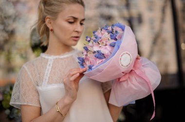 Kız pembe ve mavi çiçekler Buket ile duruyor