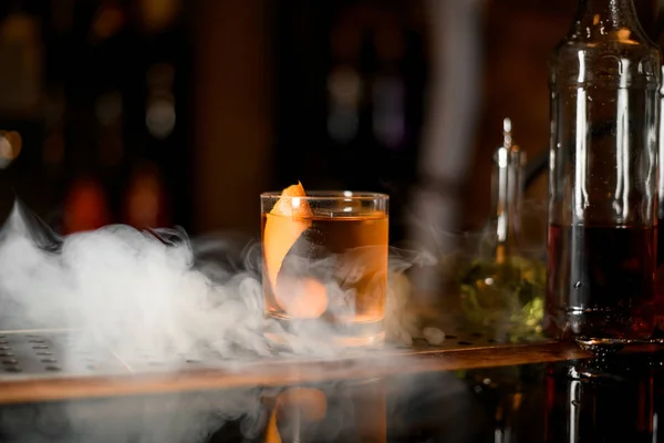 Glass of whiskey with ice and zest in steam — Stock Photo, Image