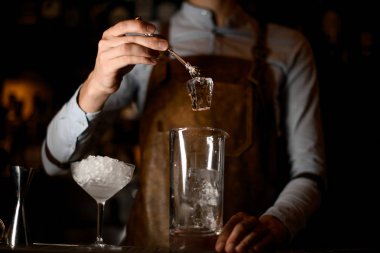 Barmen maşa ile kokteyl cam buz ekleyerek