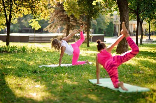 Zwei Frauen praktizieren Yoga im Park in Halbbogen-Pose. — Stockfoto
