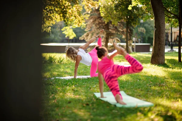 Zwei Mädchen praktizieren Yoga im Park in Halbbogen-Pose. — Stockfoto