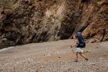 Sırt çantası ve yürüyüş çubukları ile kız çakıl sahilde yürüyüş