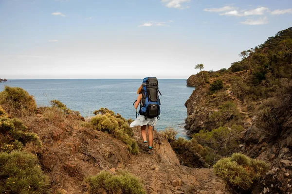 Back View Girl med en vandring ryggsäck stående på klippan på havskusten — Stockfoto