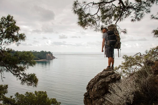 Чоловік з рюкзаком стоїть на скелі серед гілок дерев — стокове фото
