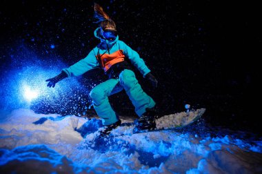 Aktif kadın snowboardcu bir turuncu ve mavi spor giyim dağ yamaç üzerinde atlama giymiş