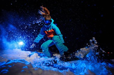 Aktif kadın snowboardcu kar yamaç üzerinde atlama turuncu ve mavi spor giyim giymiş