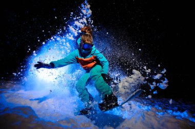 Aktif kadın snowboardcu bir turuncu ve mavi spor spor kar üzerinde atlama giymiş