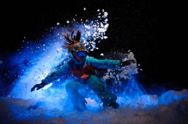 Turuncu ve mavi spor giyim giymiş aktif kadın snowboardcu kar üzerinde hileler yapar
