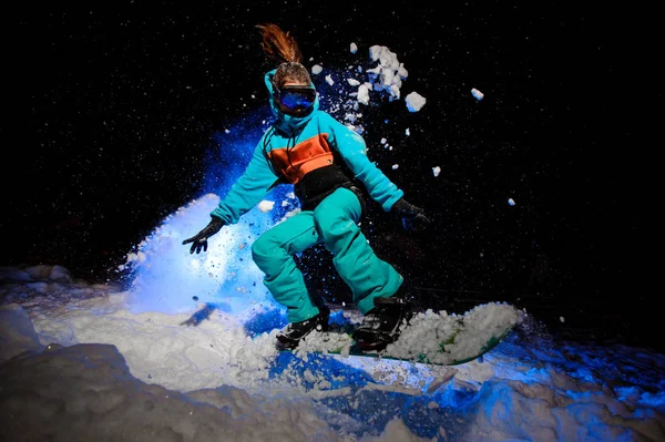 Snowboarderin in orangefarbener und blauer Sportbekleidung springt im Schnee — Stockfoto