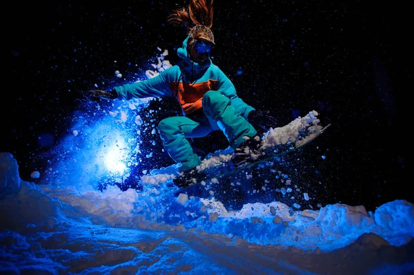 Γυναίκα χιονοοικότροφος ντυμένος σε ένα πορτοκαλί και μπλε αθλητικά είδη εκτελεί κόλπα στο χιόνι — Φωτογραφία Αρχείου