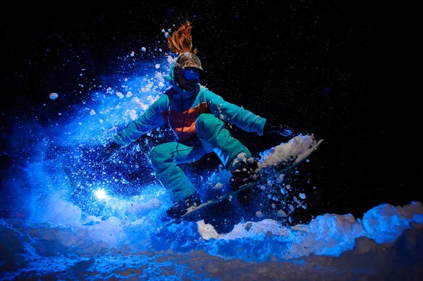 Сноубордистка, одетая в оранжевую и синюю спортивную одежду и выполняющая трюки на снегу — стоковое фото
