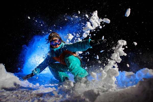 Сноубордистка в оранжевой и синей спортивной одежде делает трюки на снегу — стоковое фото