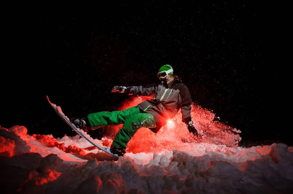 Активна жінка сноубордистка в зеленому спортивному одязі виконує трюки на гірському схилі — стокове фото