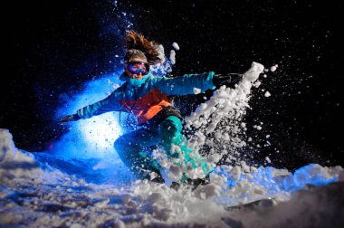 Turuncu ve mavi spor giyim giymiş snowboarder kız kar üzerinde hile yapma