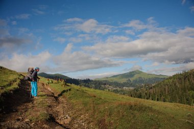 Adam yürüyüş sırt çantası ve ağaç kaplı tepelerin arka planda sopaile toprak yolda duran