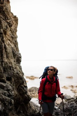 Yürüyüş sırt çantası ile denizde kıyı şeridinde kayalar arasında yürüyen kadın