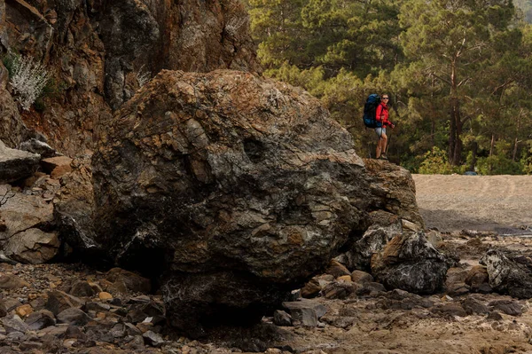 Дівчина стоїть на скелі з пішохідним рюкзаком і палицями — стокове фото