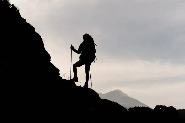 Silhouette slim girl standing on the rocks with hiking backpack and walking sticks — Stock Photo, Image