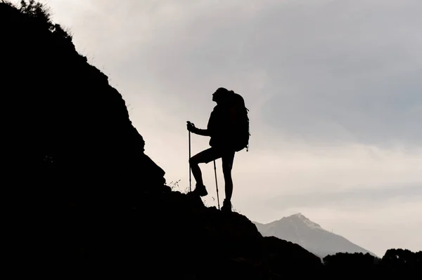 Силуэт женщина стоит на скалах с рюкзаком и трости — стоковое фото