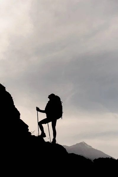 Mörk silhuett flicka stående på klipporna med vandring ryggsäck och promenadkäppar — Stockfoto