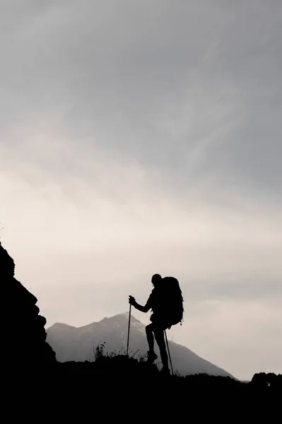 Силуэт стройная девушка, стоящая на скале с рюкзаком и ходячими палками — стоковое фото