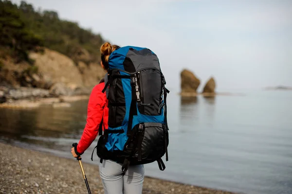 Vista trasera chica en ropa deportiva caminando cerca del mar con mochila de senderismo —  Fotos de Stock