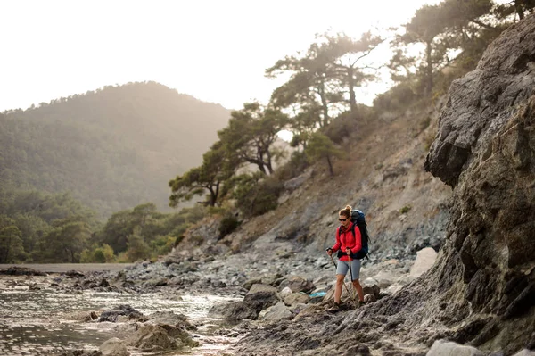 苗条适合的女孩走在海边的岩石与徒步旅行背包 — 图库照片