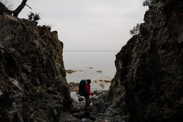 ผู้หญิงยืนอยู่ระหว่างหินบนชายฝั่งบนทะเลพร้อมกระเป๋าเป้สะพายหลังเดินป่า — ภาพถ่ายสต็อก