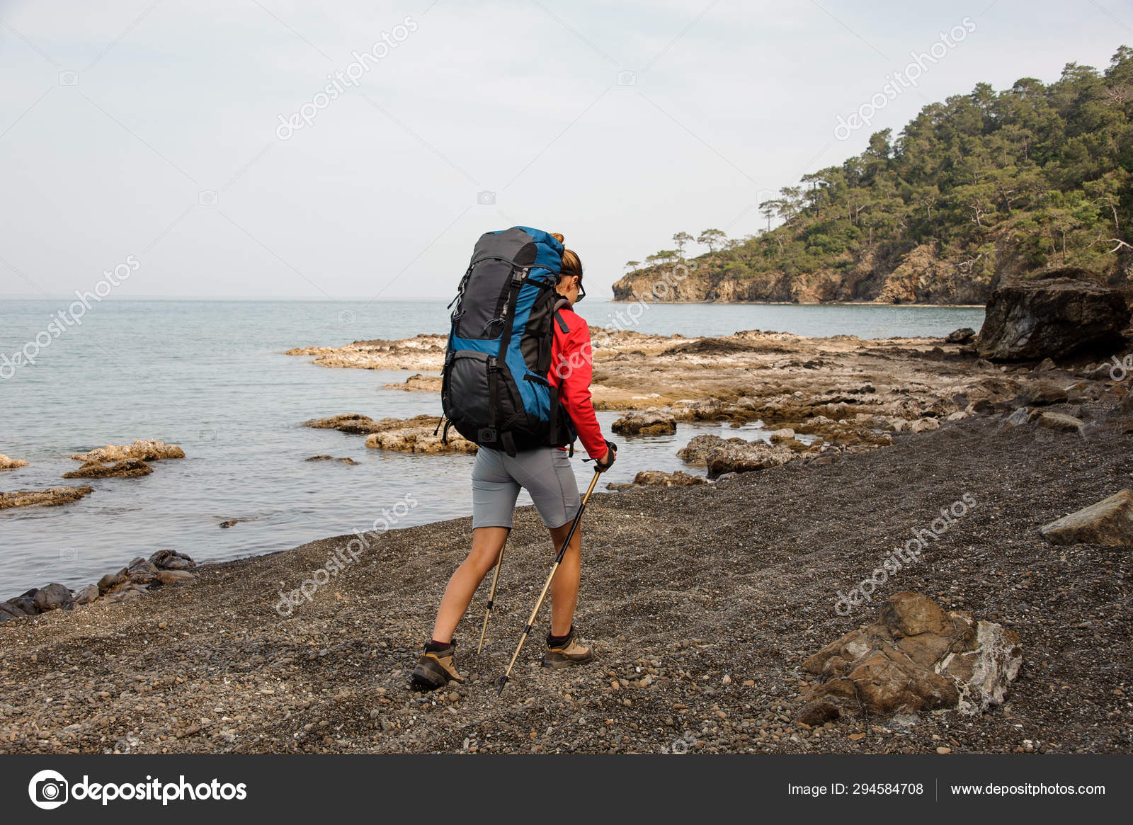 Mujer en ropa especial de pie con mochila de senderismo y palos en la roca