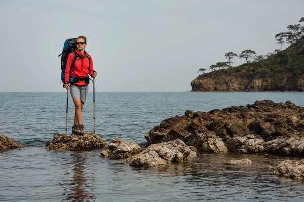 Meisje in zonnebril staande op de rots op de zee met wandelrugzak — Stockfoto