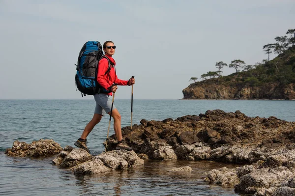 Deportiva mujer caminando sobre la roca en el mar con mochila de senderismo —  Fotos de Stock