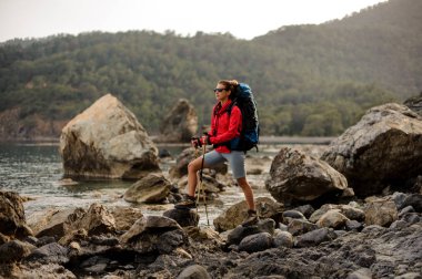 Yürüyüş sırt çantası ile denizde kıyı şeridi üzerinde kayalar üzerinde duran ince uygun kız