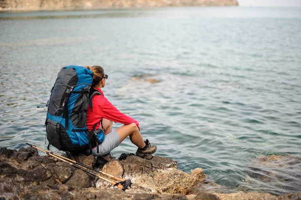 Chica sentada en las rocas con la mochila de senderismo y bastones —  Fotos de Stock