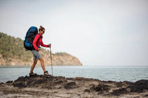 Kvinna i sportkläder gå på klippan på havet med vandring ryggsäck — Stockfoto