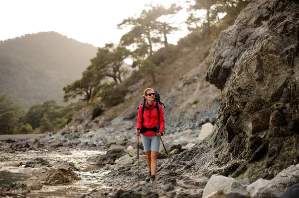 Femme mince en forme marcher sur les rochers sur la côte sur la mer avec sac à dos de randonnée — Photo