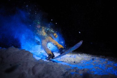 Sarı spor giyimli aktif erkek snowboardcu kar yamacında hile yapar