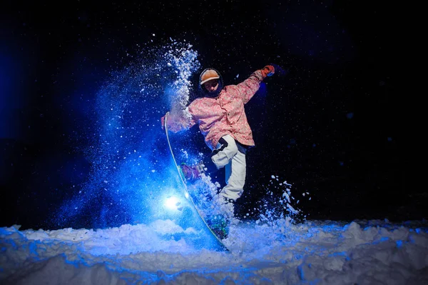 Attivo snowboarder maschile vestito con un abbigliamento sportivo bianco e rosa esegue trucchi sulla pista da neve — Foto Stock