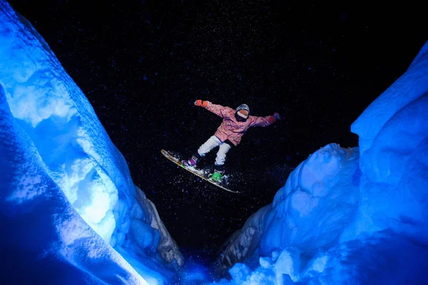 Aktiver männlicher Snowboarder in weißer und pinkfarbener Sportbekleidung springt zwischen den Schneehängen — Stockfoto