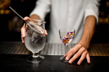Barmen bir süzgeç ve çiçek dekore cam ile bir kokteyl ölçüm fincan tutan