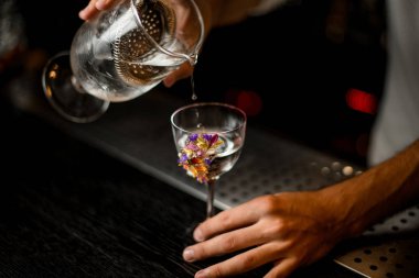 Erkek barmen çiçeklerle süslenmiş bir bardağa bir süzgeç ile ölçüm fincan bir kokteyl dökme