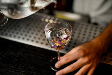 Barmen çiçeklerle süslenmiş bir bardağa bir süzgeç ile ölçüm fincan bir kokteyl dökme