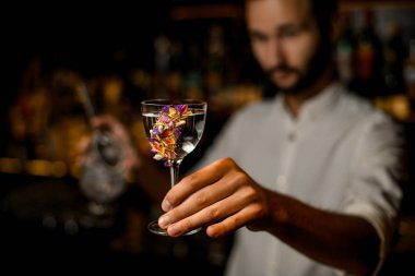 Çiçeklerle süslenmiş camda kokteyl servis eden çekici bulanık barmen