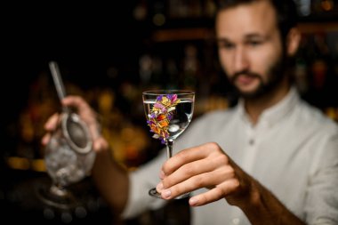 Erkek bulanık barmen çiçeklerle süslenmiş cam bir kokteyl hizmet
