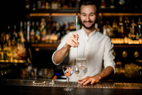 Barista sorridente che mescola un cocktail con un cucchiaio in primo piano del vetro decorato con fiori — Foto Stock